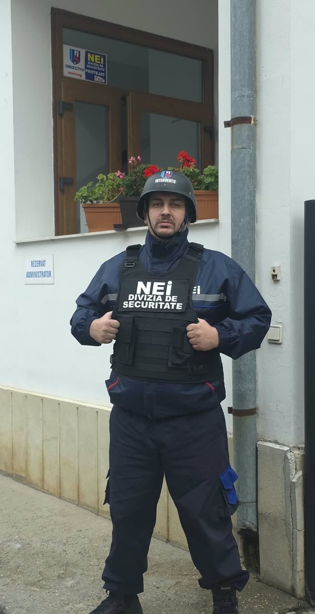 Agent NEI cu cască și vestă de protecție, în fața unei clădiri