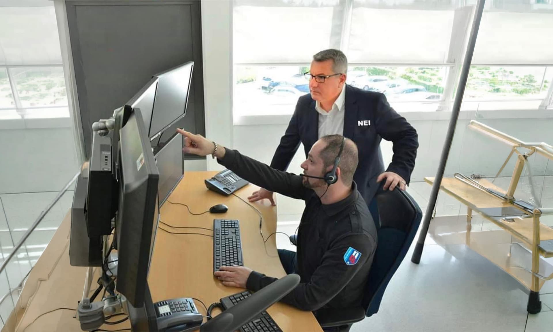 Dispeceratul NEI: un operator cu cască arată spre monitoare, lângă un coleg