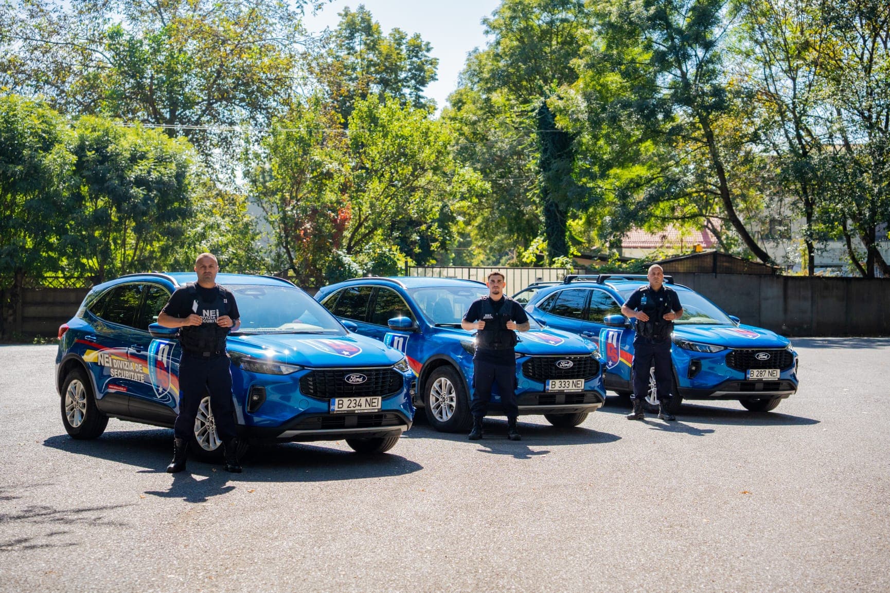 Trei agenți de intervenție NEI lângă trei autovehicule Ford cu însemnele companiei