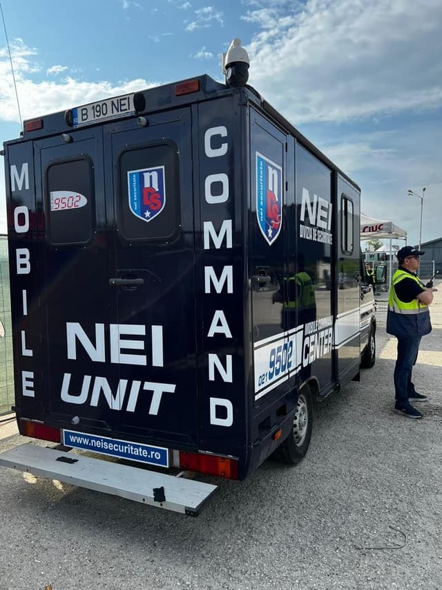 Autospeciala Mobile Command Unit a NEI, cu o cameră pe acoperiș și un agent alături