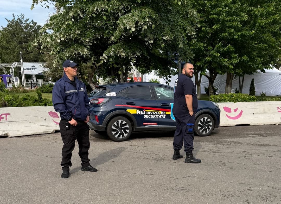 Doi agenți de pază NEI la un eveniment, lângă autovehiculul companiei